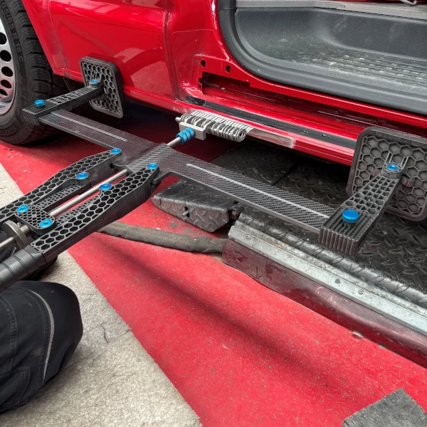 Modernes Richtwerkzeug für Karosseriereparatur an rotem Auto in Werkstatt im Einsatz.