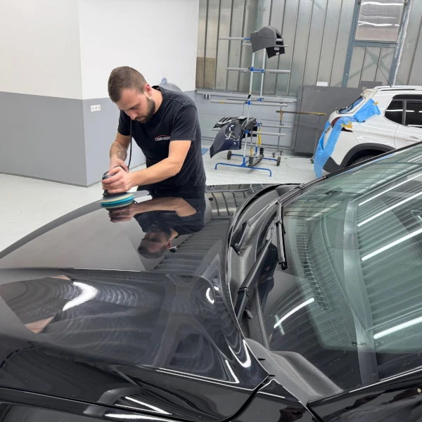 Ein Mann poliert in einer Werkstatt die Motorhaube eines Autos für professionelle Autopflege.