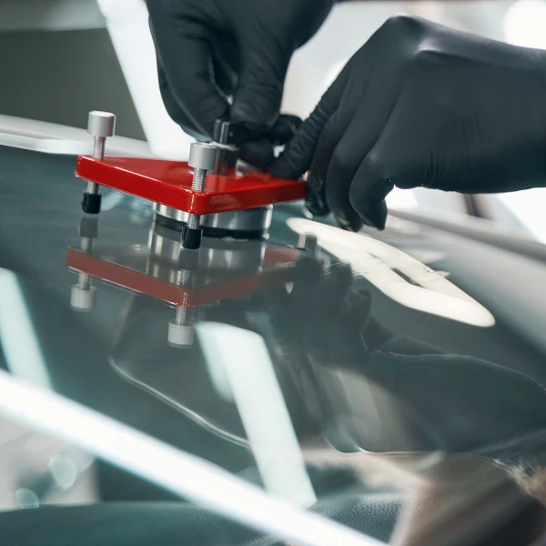 Ein Techniker repariert mit Spezialwerkzeug eine beschädigte Autoscheibe in der Werkstatt.