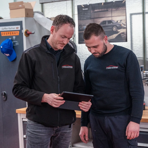 Zwei Kfz-Mechaniker besprechen Reparaturdetails in einer Autowerkstatt am Tablet.