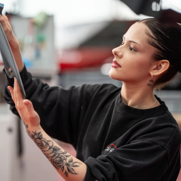 Junge Frau mit Tattoo arbeitet konzentriert am Tablet in moderner Werkstattumgebung.