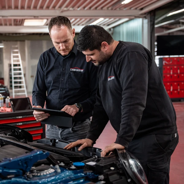 Zwei Kfz-Mechaniker inspizieren ein Auto in einer modernen Autowerkstatt mit Tablet.