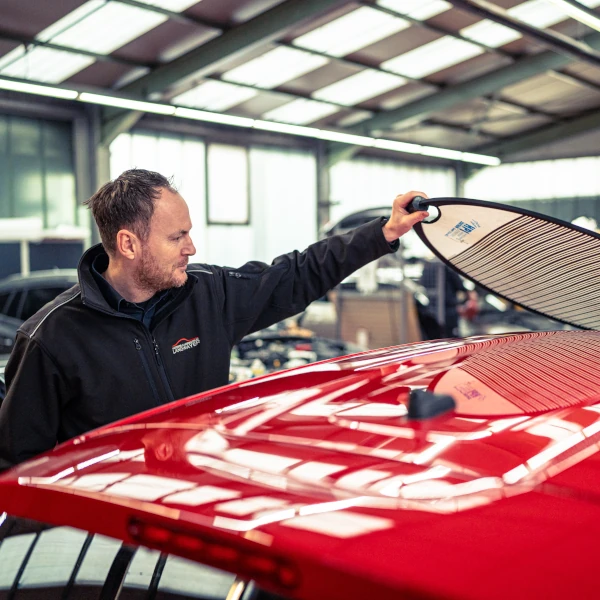 Mann legt Surfbrett auf roten Autodachträger in moderner Werkstatt für Outdoor-Aktivitäten.