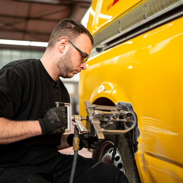 Ein Mechaniker repariert eine beschädigte Autotür an einem gelben Transporter in der Werkstatt.