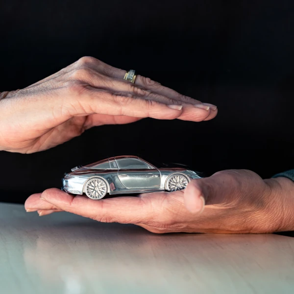 Zwei Hände schützen ein Modellauto als Symbol für Kfz-Versicherung und Autoschutz.
