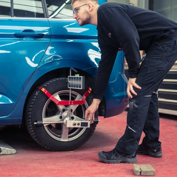 KFZ-Mechaniker prüft mit Achsvermessungsgerät die Spur eines blauen Autos in Werkstatt.